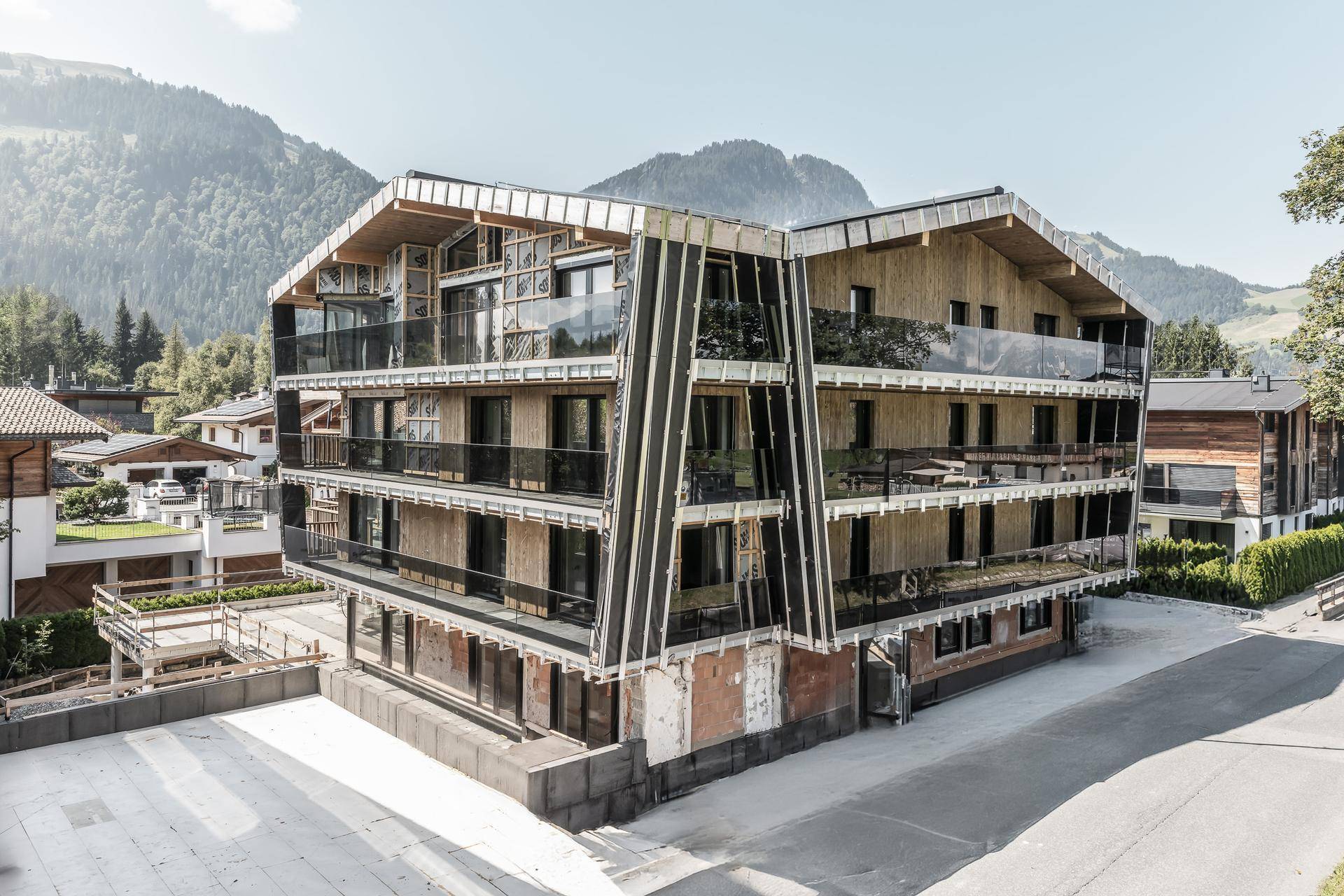 Moderne Architektur mit Holzfassade und Glasbalkonen, eingebettet in eine Berglandschaft.