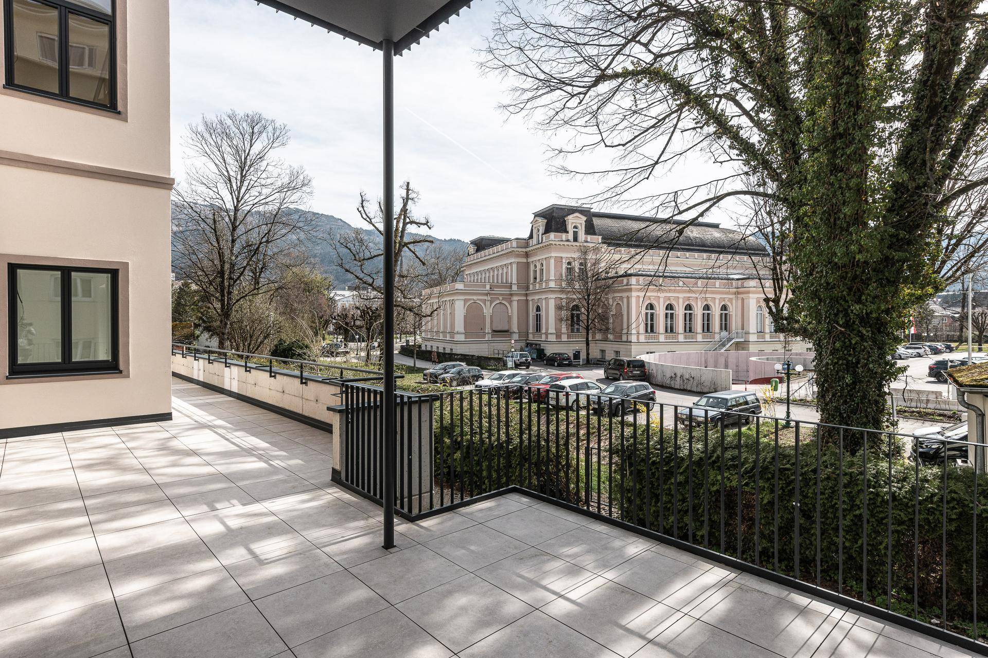 Geräumige Außenterrasse mit Fliesenboden und Blick auf ein historisches Gebäude und die Berge.