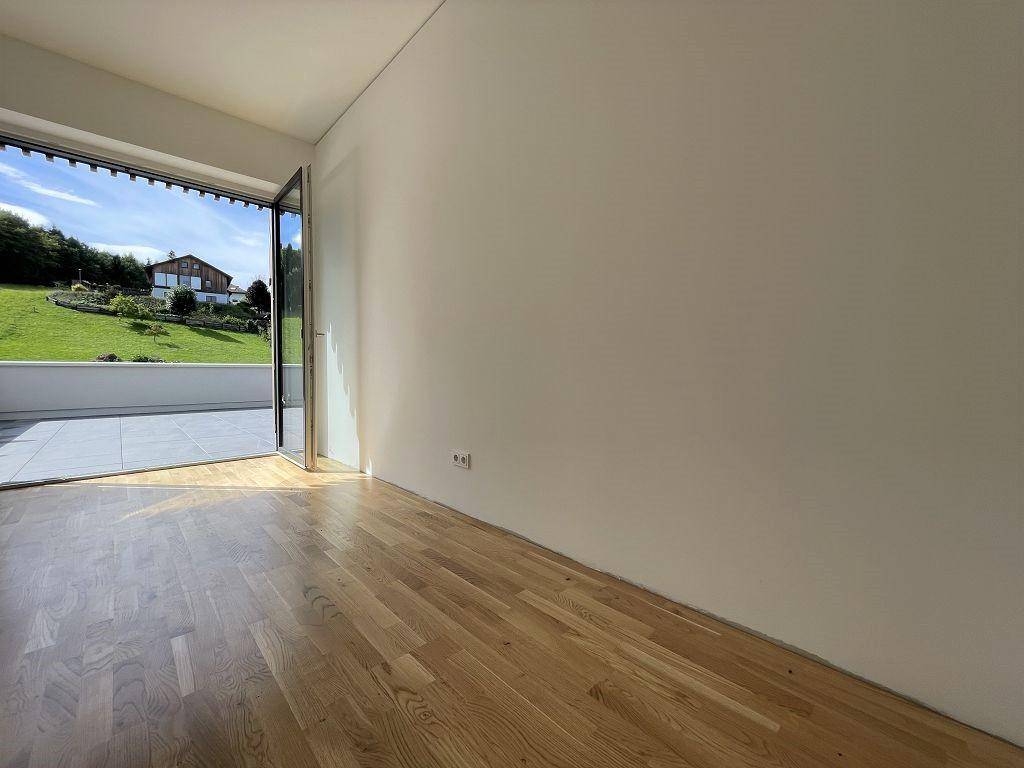 Lichtdurchfluteter Raum mit Holzboden und Zugang zu einer Terrasse mit Blick auf die grüne Umgebung.