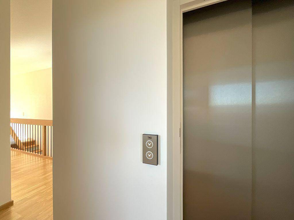 Heller Flur mit Zugang zu einem modernen Aufzug und Blick auf die Treppe.