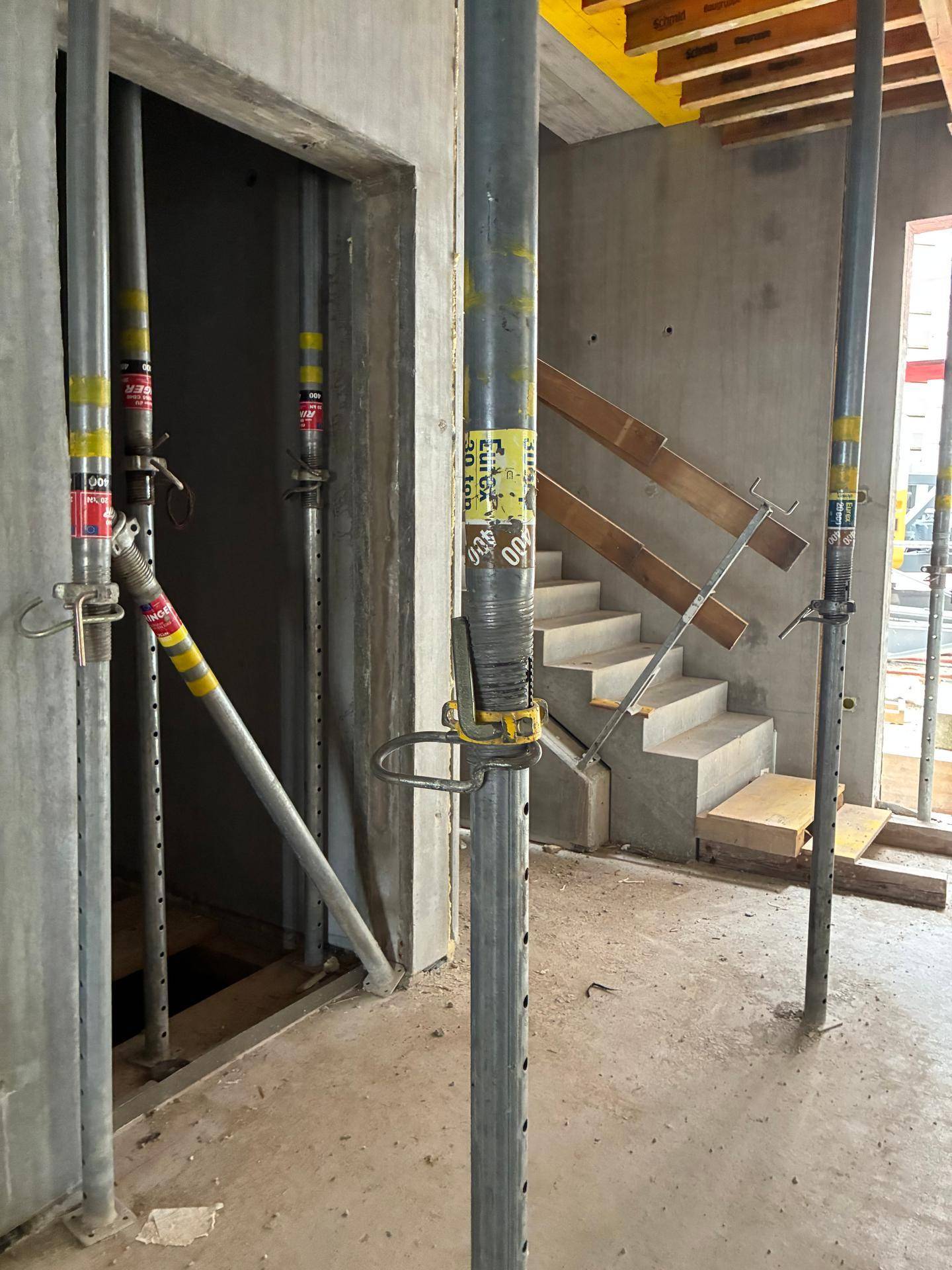 Innenbereich eines Rohbaus mit Betonwänden, Metallstützen und einer Betontreppe.