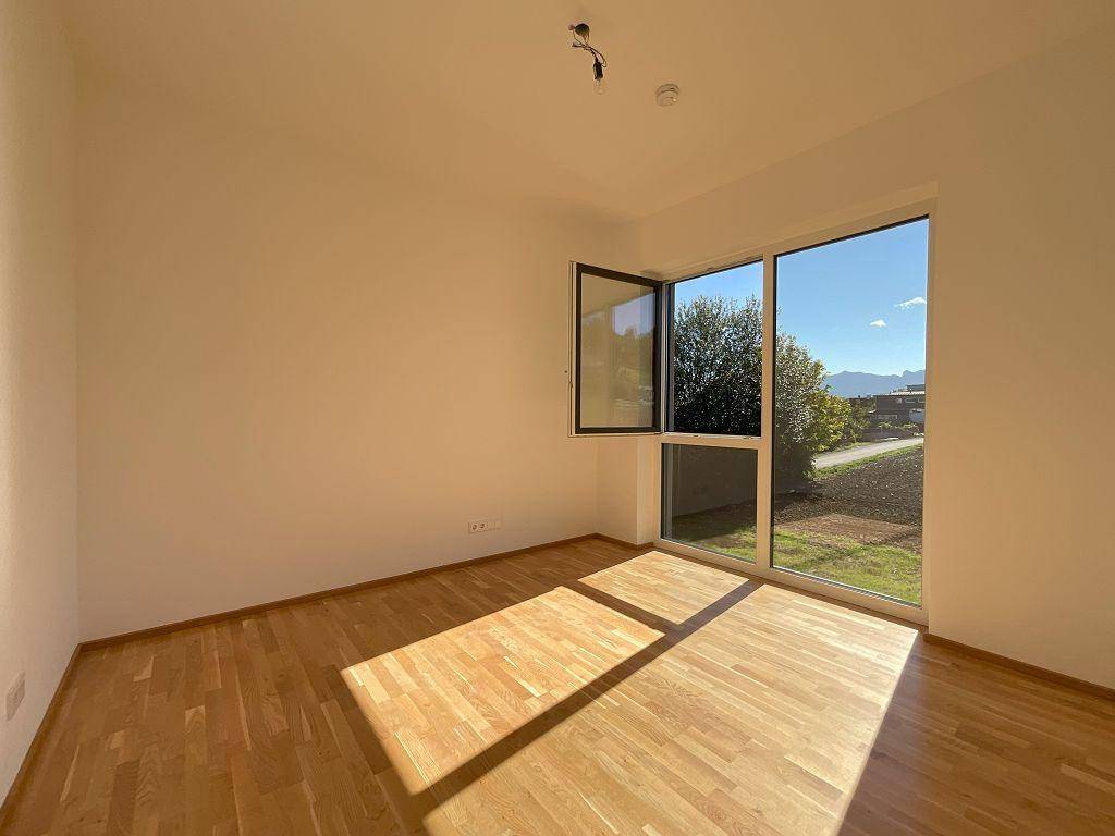 Leerer Raum mit Holzboden, großen Fenstern und viel Tageslicht.