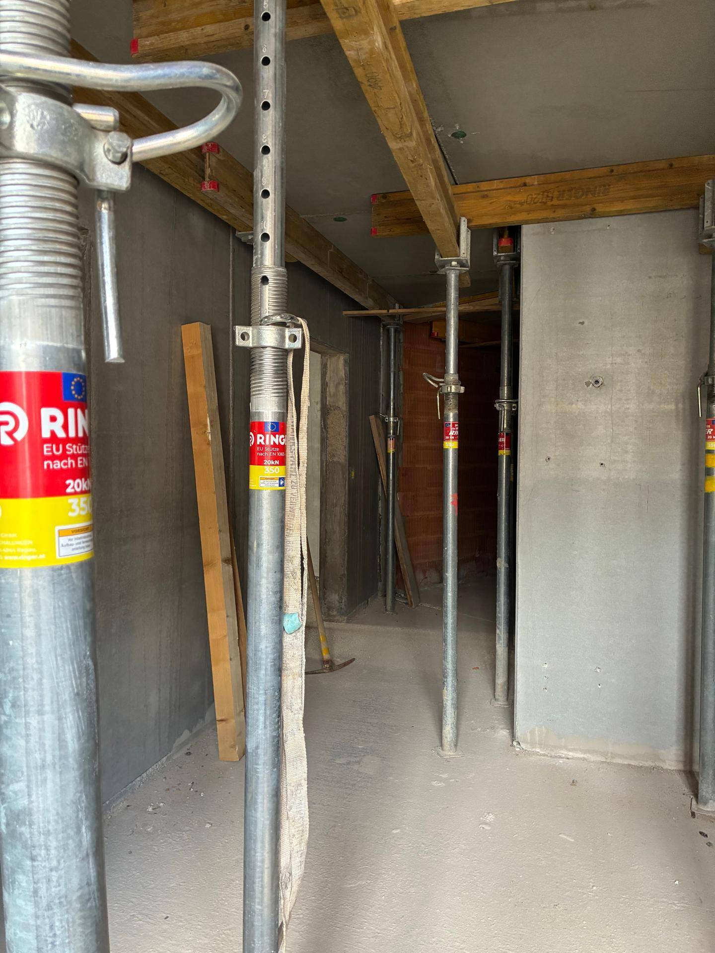 Innenansicht eines Rohbaus mit Betonwänden und Metallstützen für die Deckenkonstruktion.