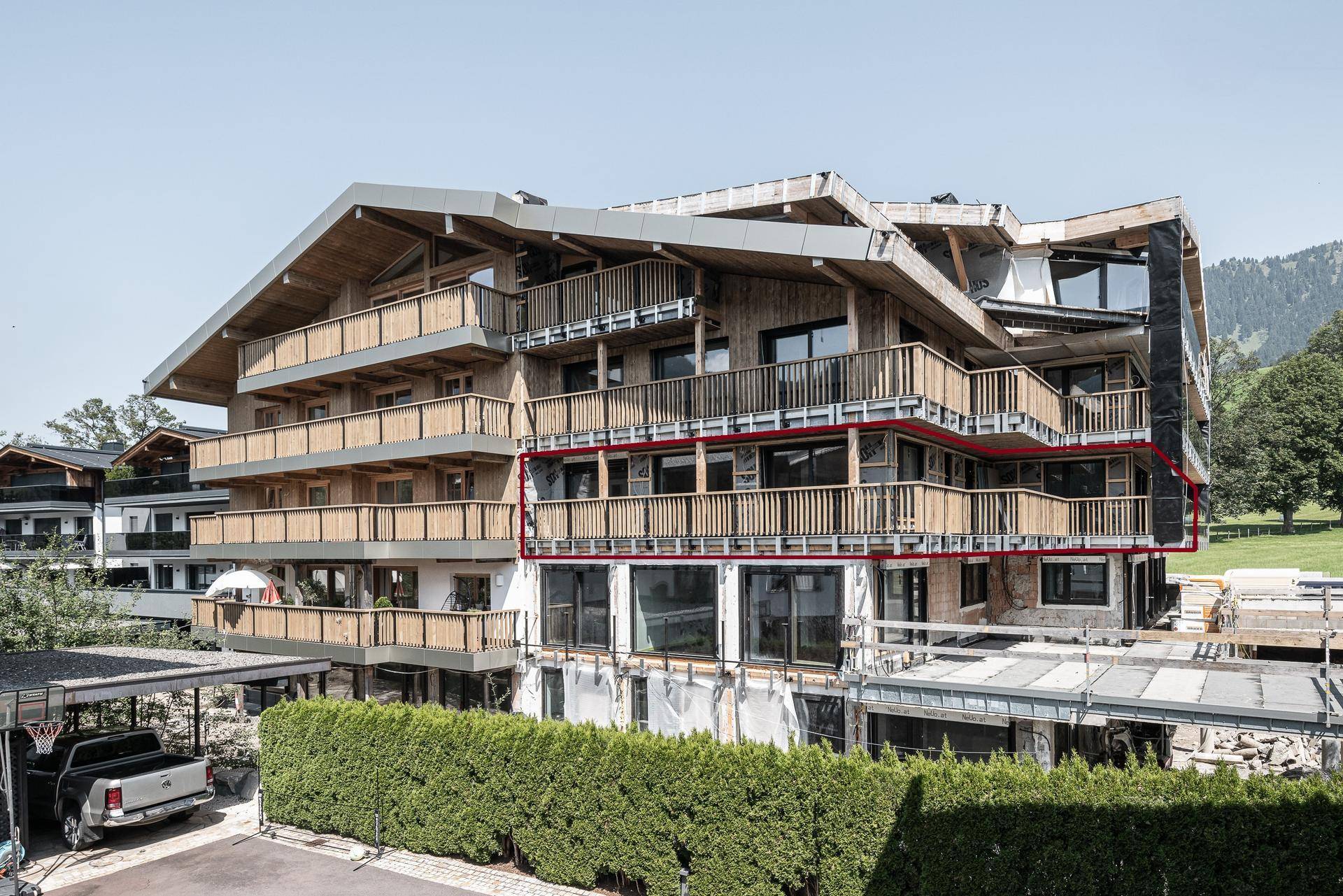 Rückansicht des modernen Apartmentkomplexes mit Holzfassade und mehreren Balkonen, umgeben von Grünflächen.