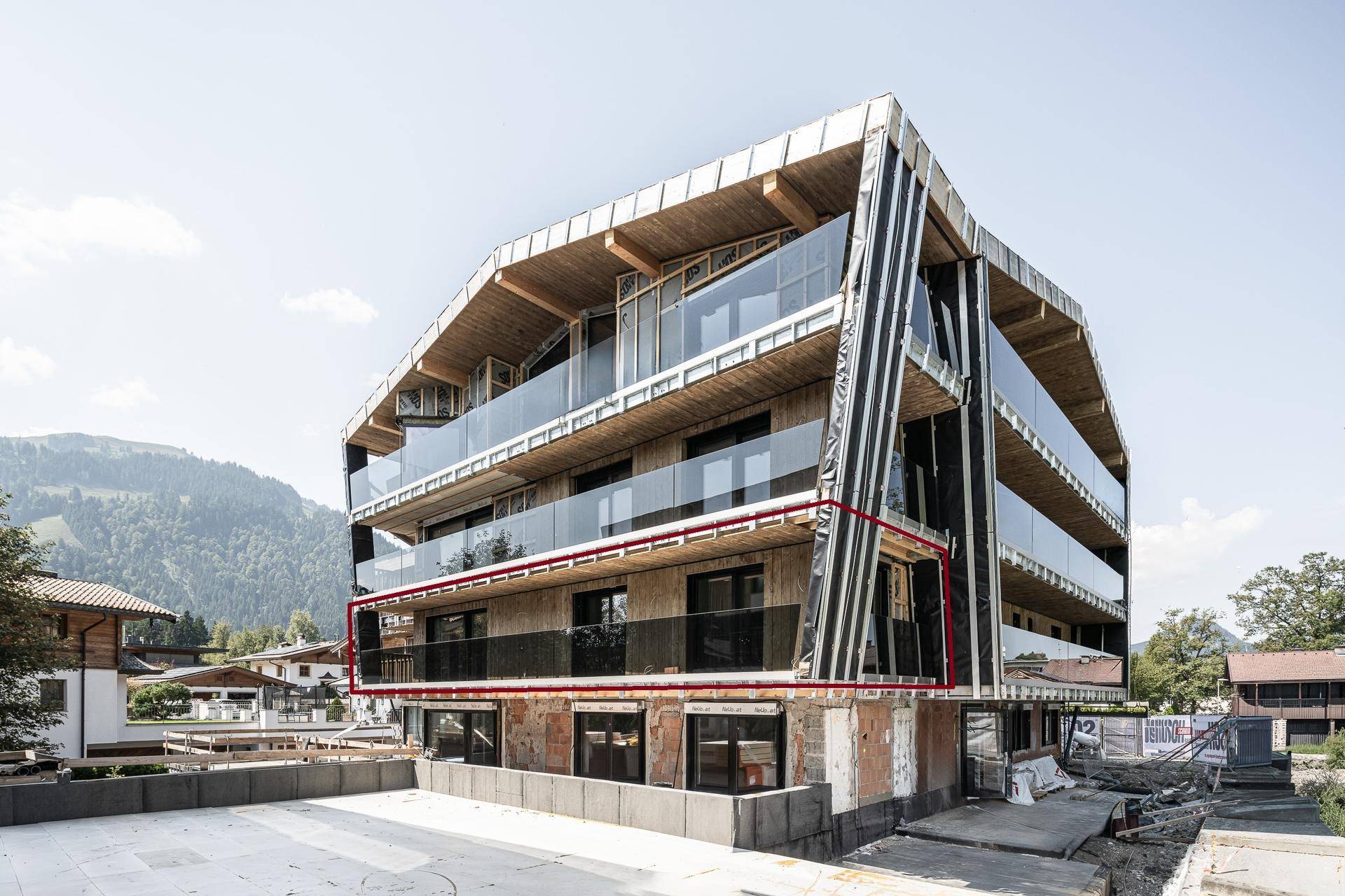 Neubau-Apartmenthaus mit moderner Holz-Glas-Fassade und Balkonen vor alpiner Kulisse.
