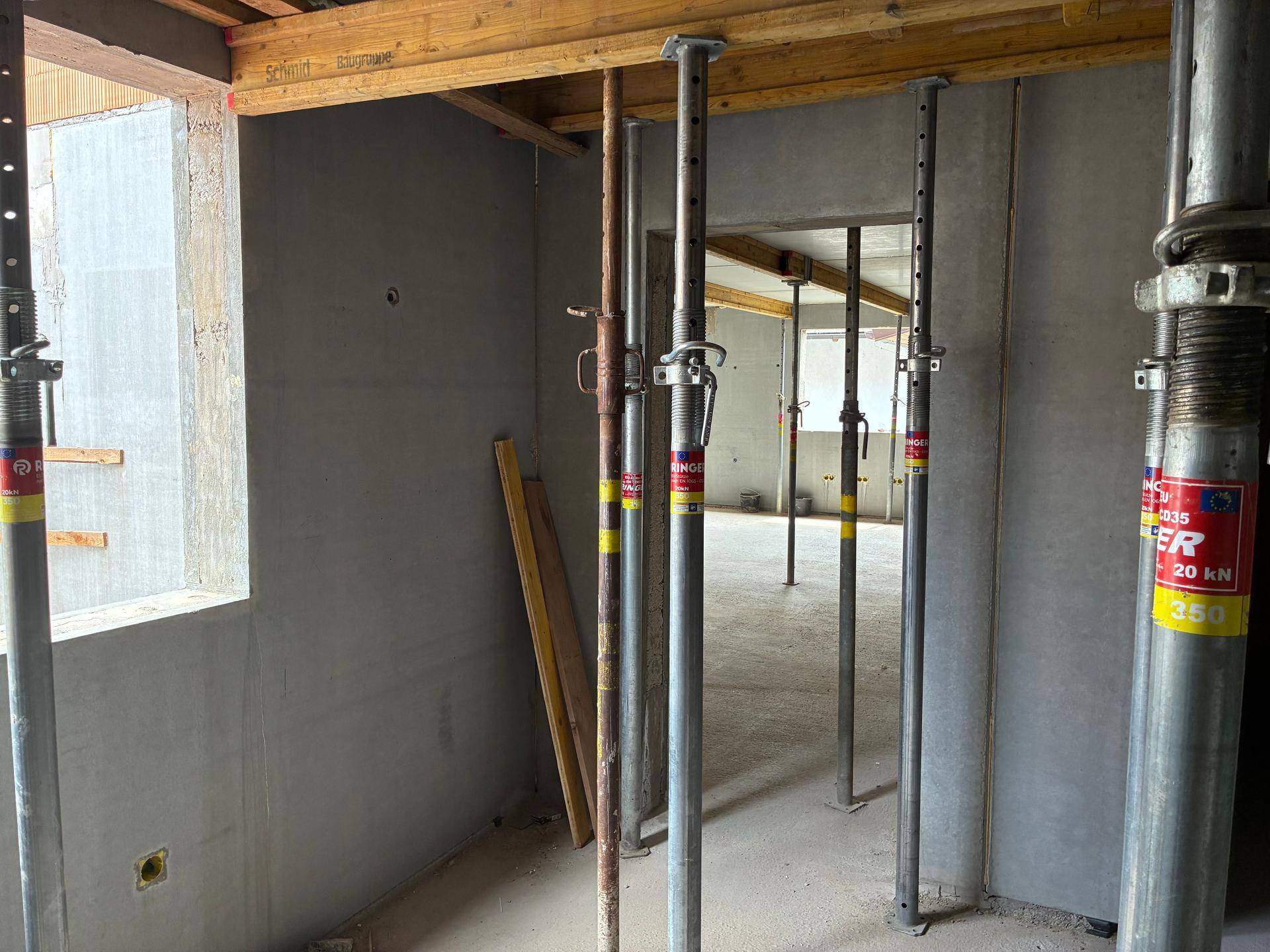 Rohbau mit Betonwänden und zahlreichen Metallstützen zur Deckenschalung.