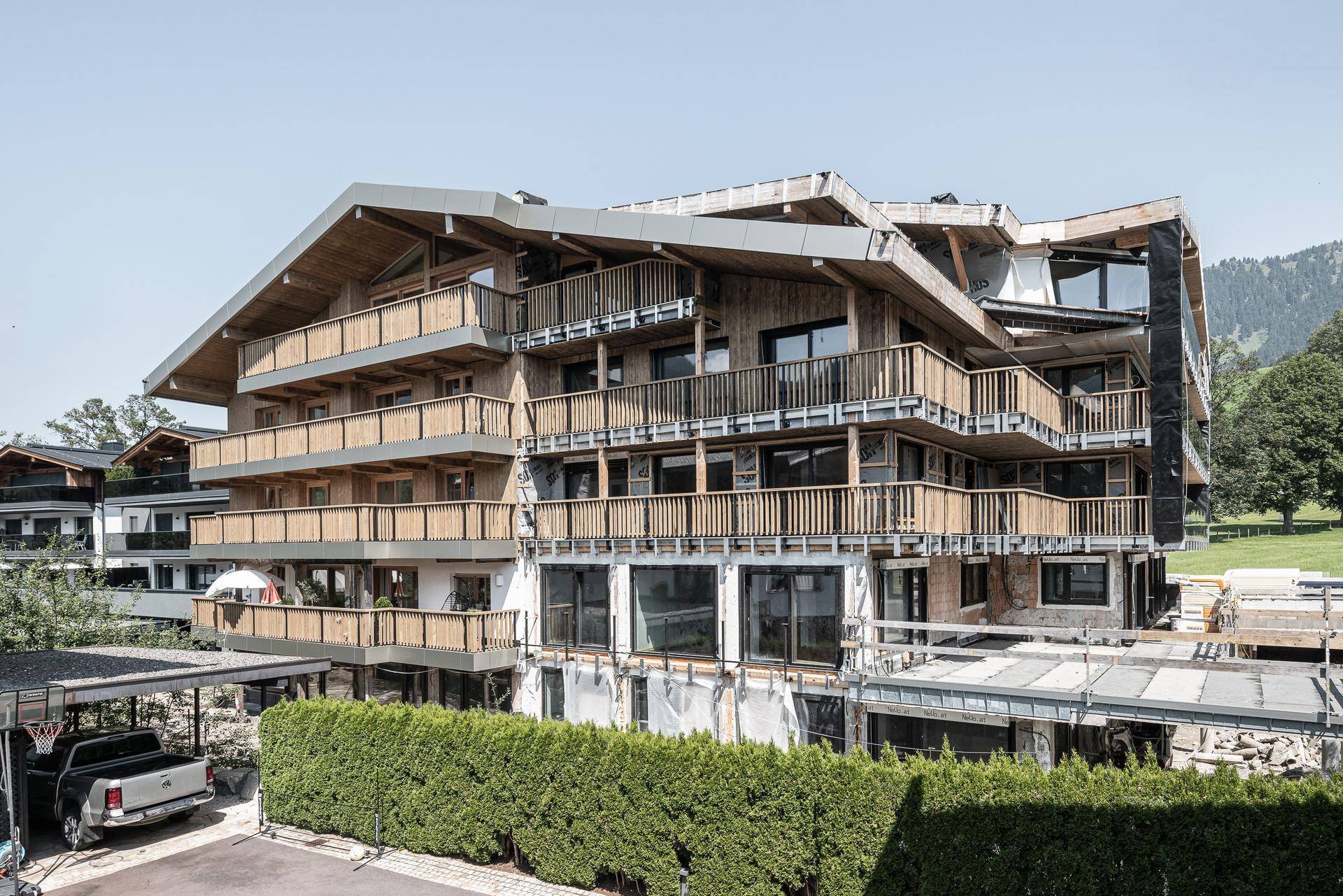 Neubau mit traditionellen Holzbalkonen und moderner Architektur in alpiner Umgebung.