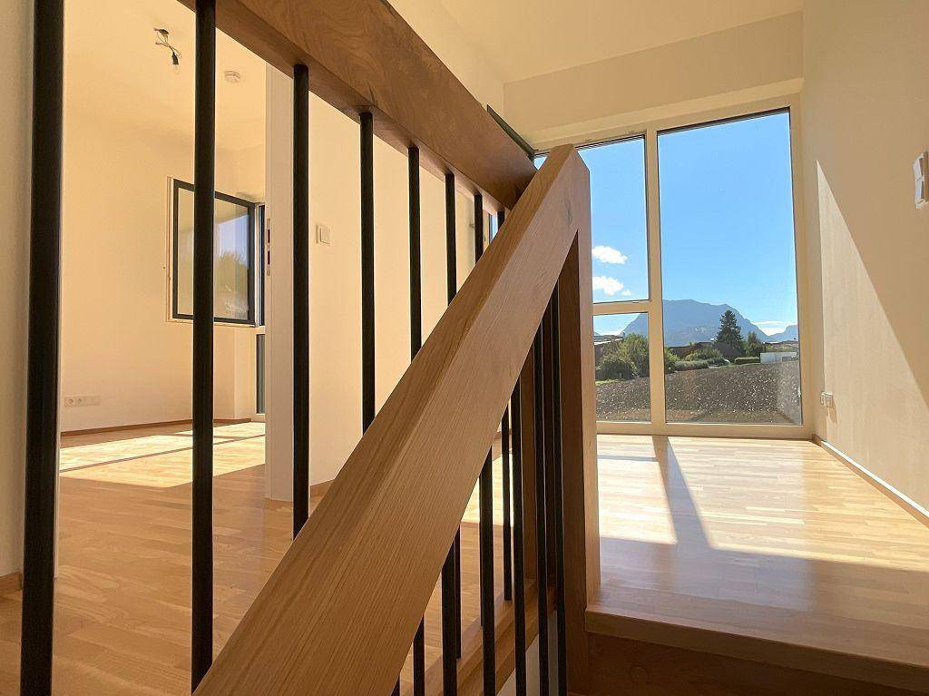 Heller Flur im Obergeschoss mit Holzboden, moderner Treppe und weitem Blick auf die Berge.