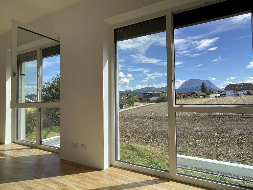 Lichtdurchfluteter Raum mit Holzboden und weitem Blick über Felder und Berge.