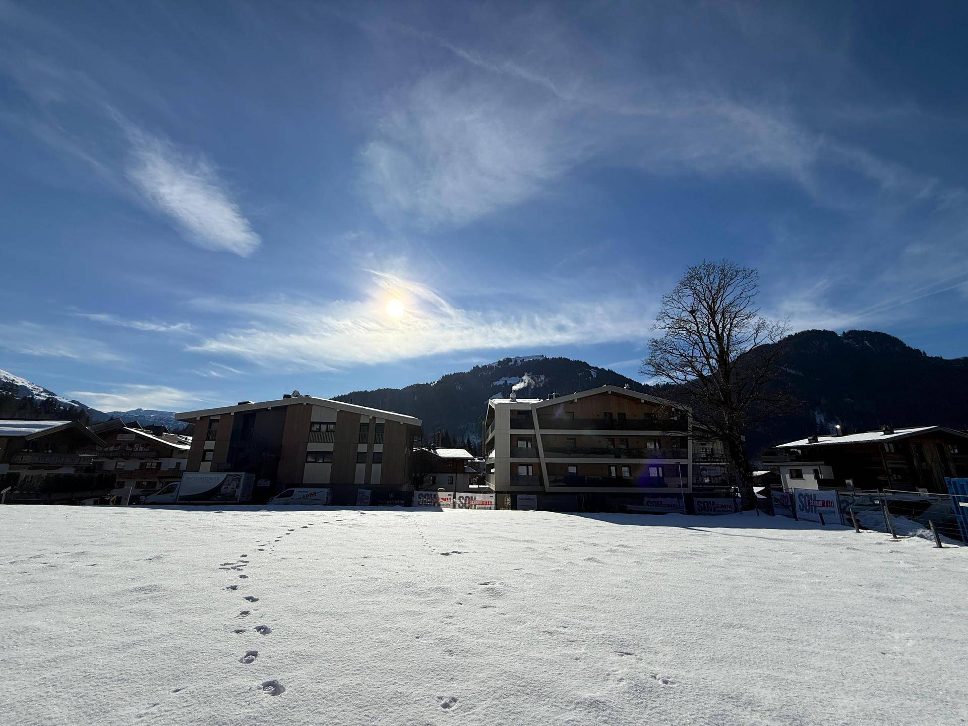 Apartmentgebäude in winterlicher Landschaft mit verschneiten Feldern und Bergen unter blauem Himmel.