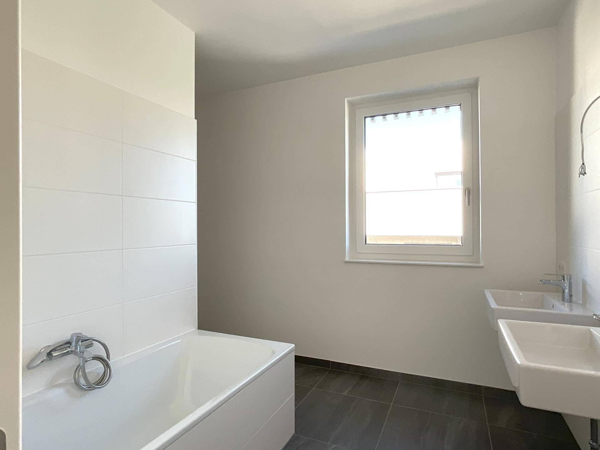 Helles Badezimmer mit Badewanne, Doppelwaschbecken und Fenster für Tageslicht.
