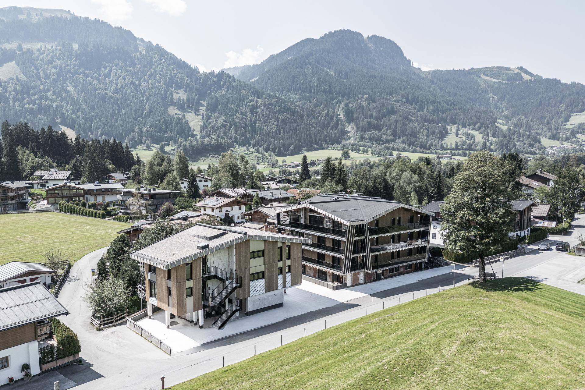Luftaufnahme eines modernen Wohnkomplexes in einer grünen Berglandschaft mit umliegenden Häusern.