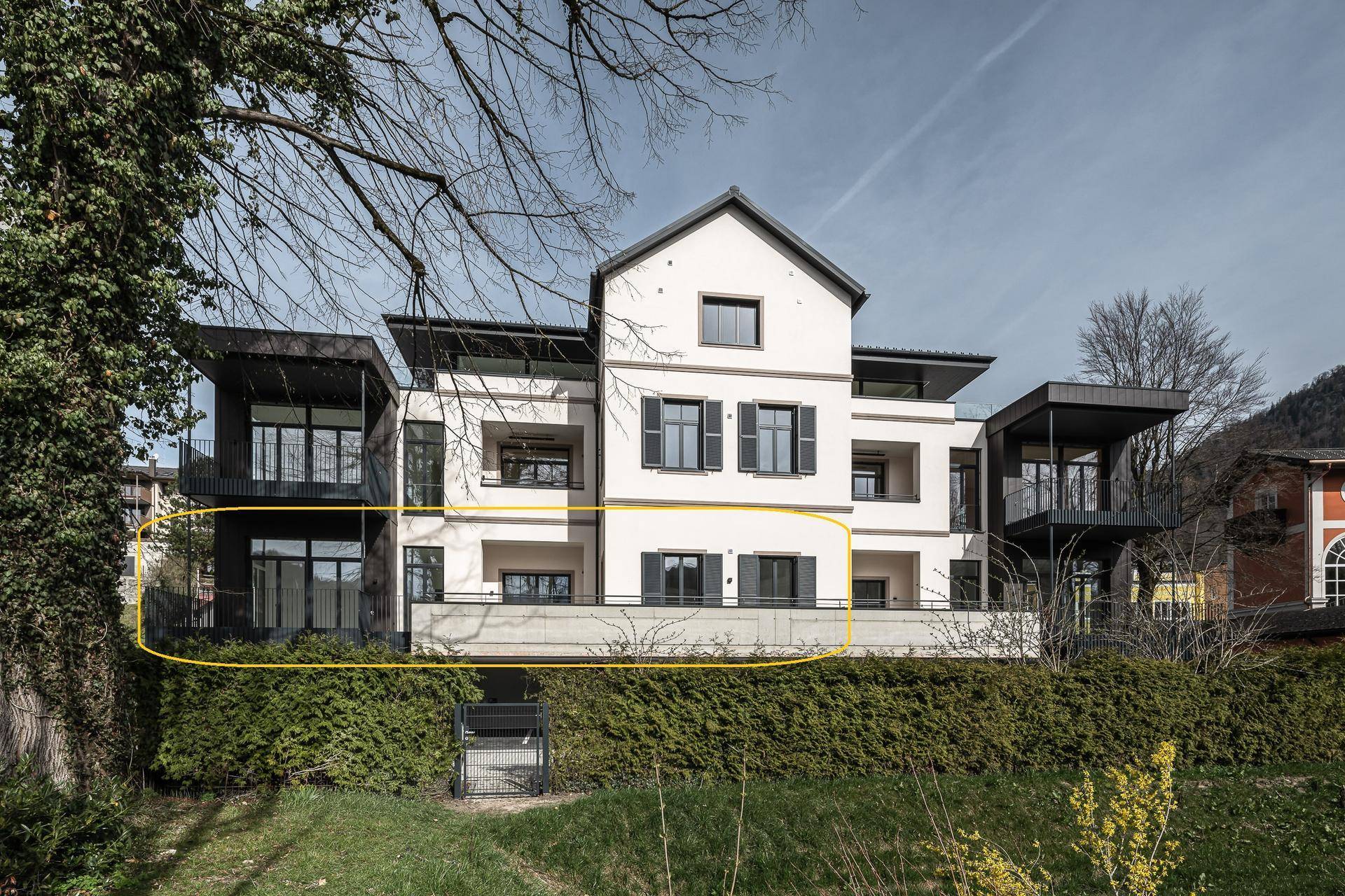 Modernes Mehrfamilienhaus mit traditionellen Elementen, großen Fenstern und Balkonen, umgeben von Grünflächen.
