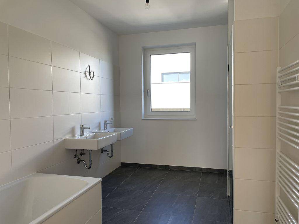 Helles, modernes Badezimmer mit Badewanne, Doppelwaschbecken, Fenster und beheiztem Handtuchhalter.