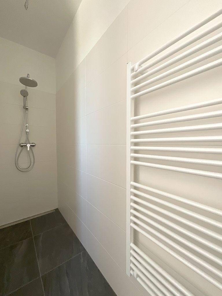 Moderne Dusche mit Regenduschkopf und beheiztem Handtuchhalter in einem hellen Badezimmer.