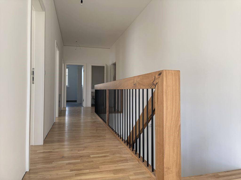 Heller Flur im Obergeschoss mit Holzboden und moderner Holztreppe mit Metallgeländer.