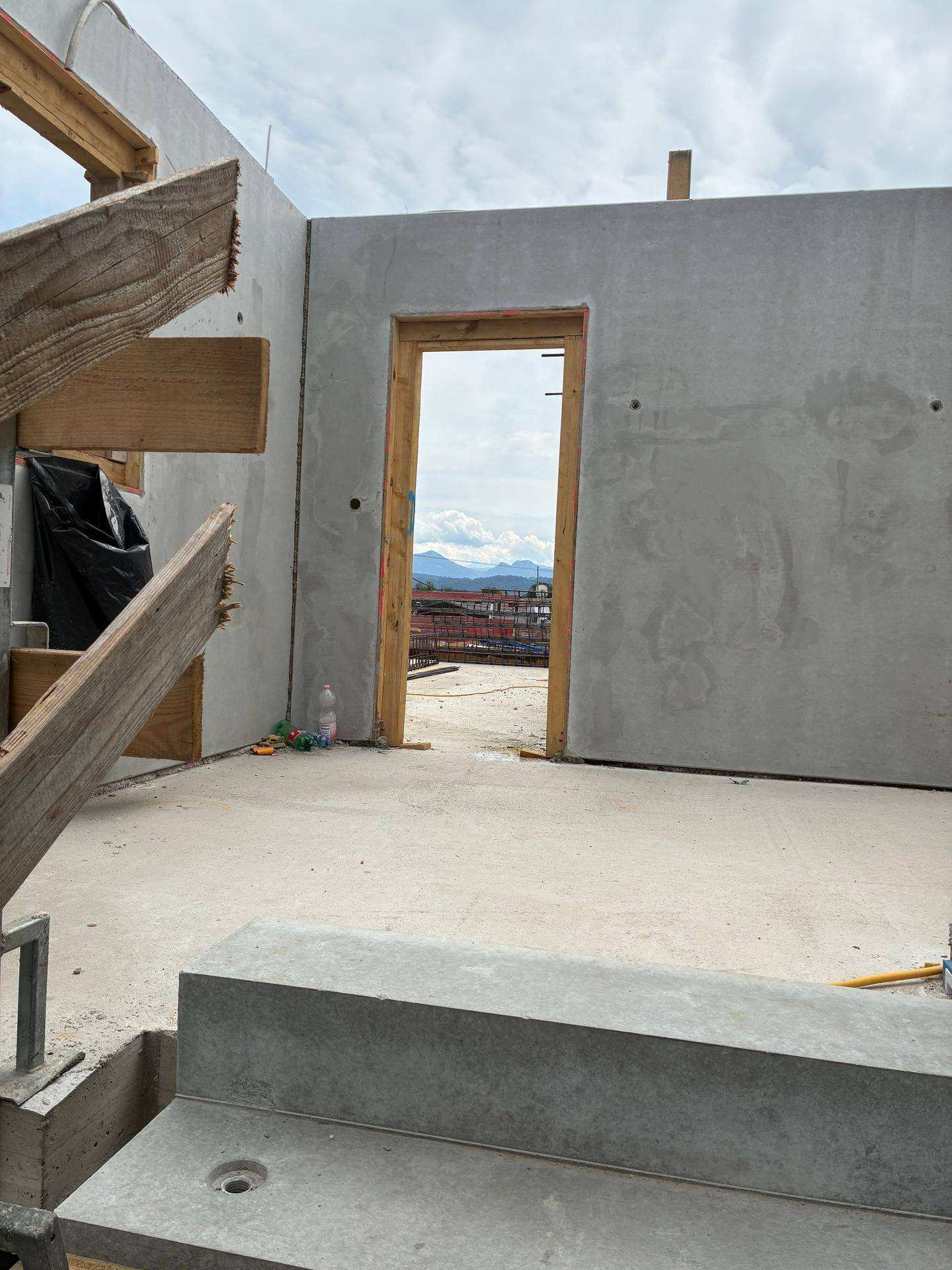 Rohbau eines Raumes mit Betonwänden und einer Türöffnung, die ins Freie führt.