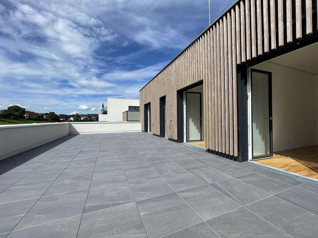 Weitläufige Dachterrasse mit grauen Fliesen und Holzfassade, ideal für Entspannung im Freien.