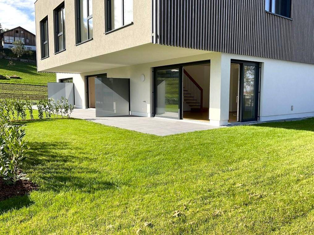 Rückseite des modernen Hauses mit Terrasse und weitläufigem Rasenbereich.