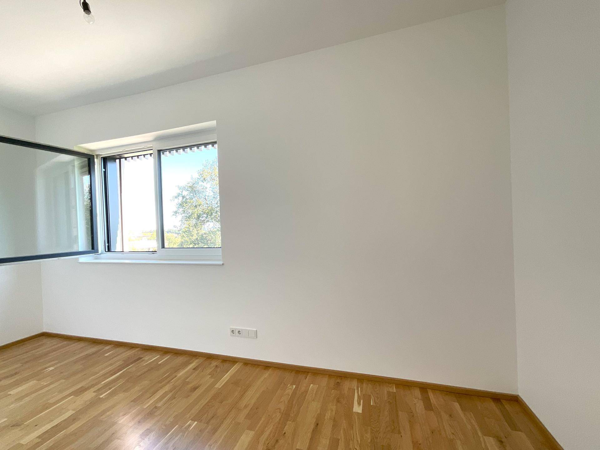 Leerer Raum mit Parkettboden und Fenster, das viel Tageslicht hereinlässt.