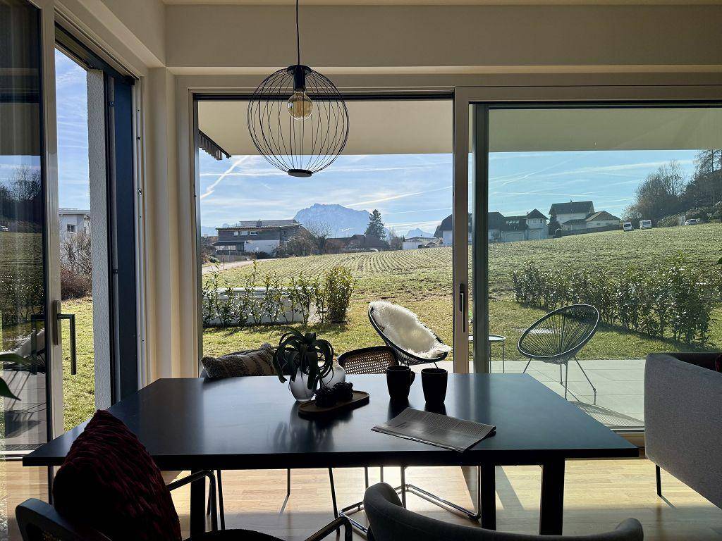 Heller Essbereich mit großem Tisch, modernen Leuchten und weitem Blick auf die umliegende Natur.
