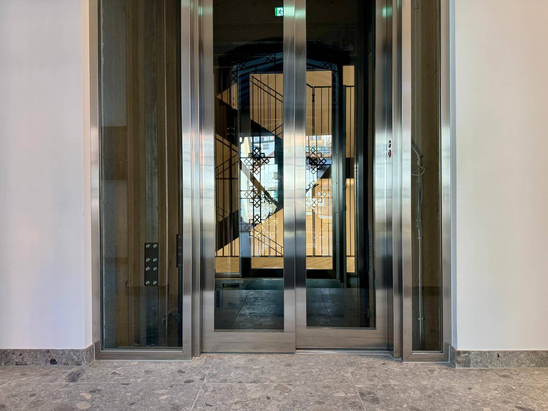 Moderner Glasaufzug im Eingangsbereich mit Blick auf das Treppenhaus.