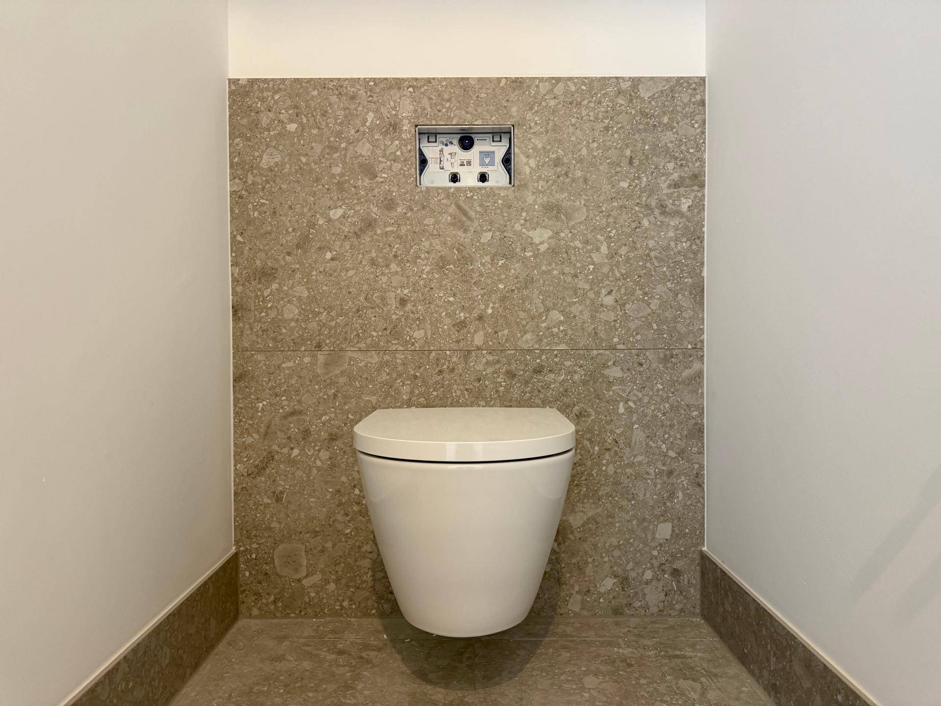 Modernes WC mit wandhängender Toilette und stilvollen Fliesen in Terrazzo-Optik.