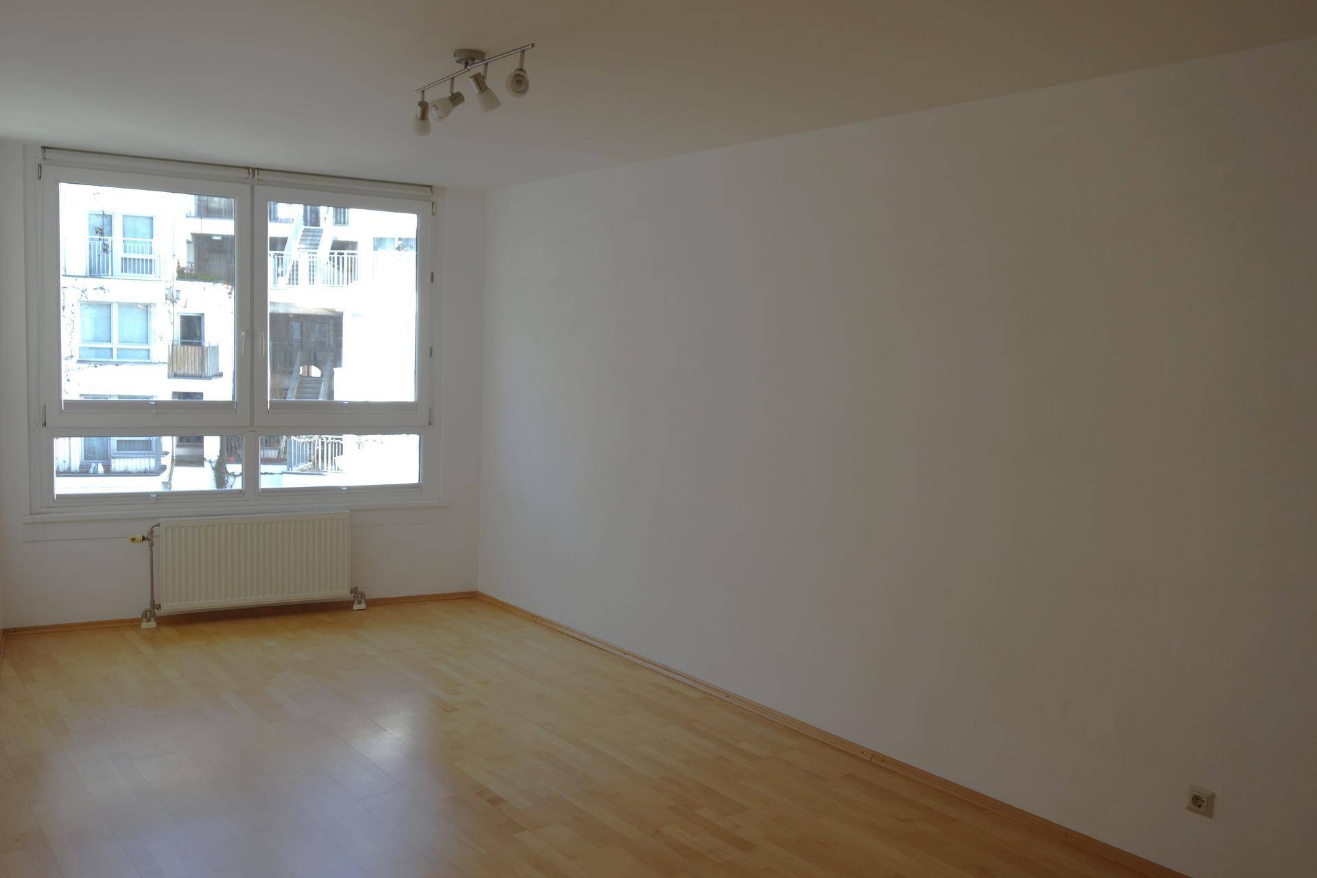 Geräumiger, heller Raum mit Holzboden und großen Fenstern, ideal als Wohnzimmer.