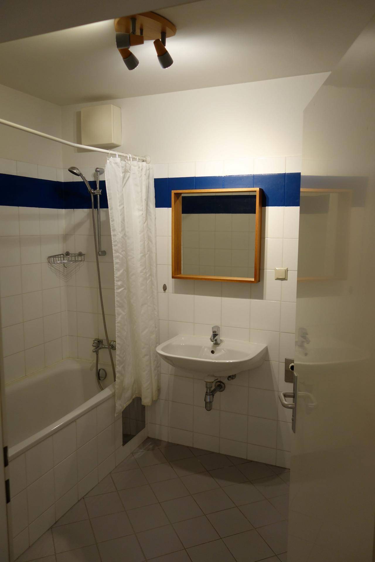Badezimmer mit Badewanne, Dusche und Waschbecken, ausgestattet mit weißen und blauen Fliesen.