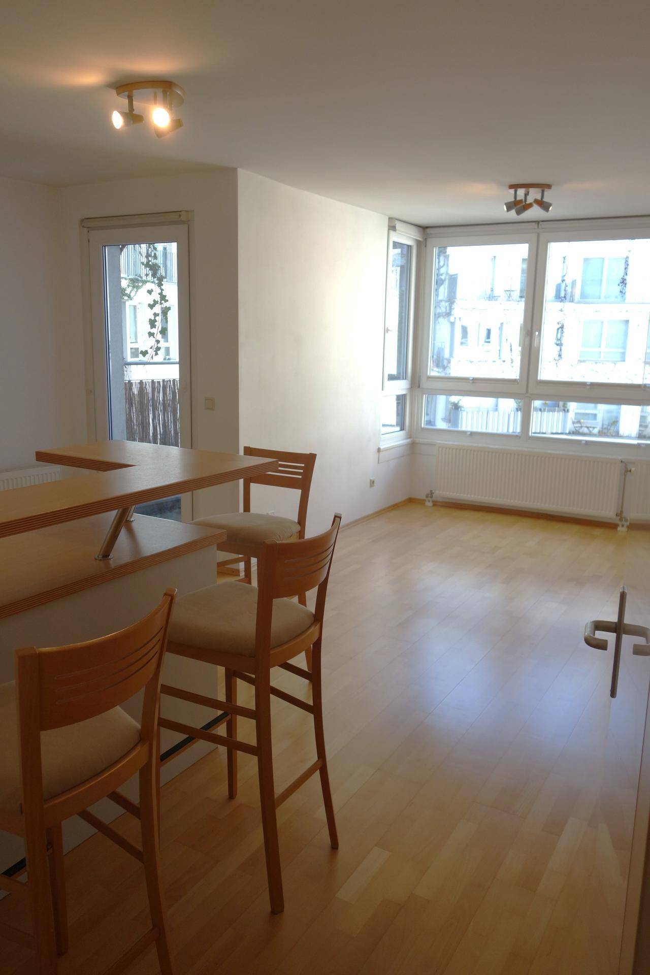 Heller Wohnbereich mit Holzboden, Frühstücksbar und Zugang zu einem kleinen Balkon.