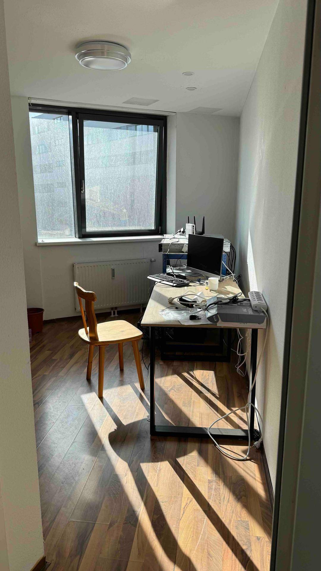 Einzelbüro mit Schreibtisch, Holzstuhl und großem Fenster, das viel natürliches Licht hereinlässt.