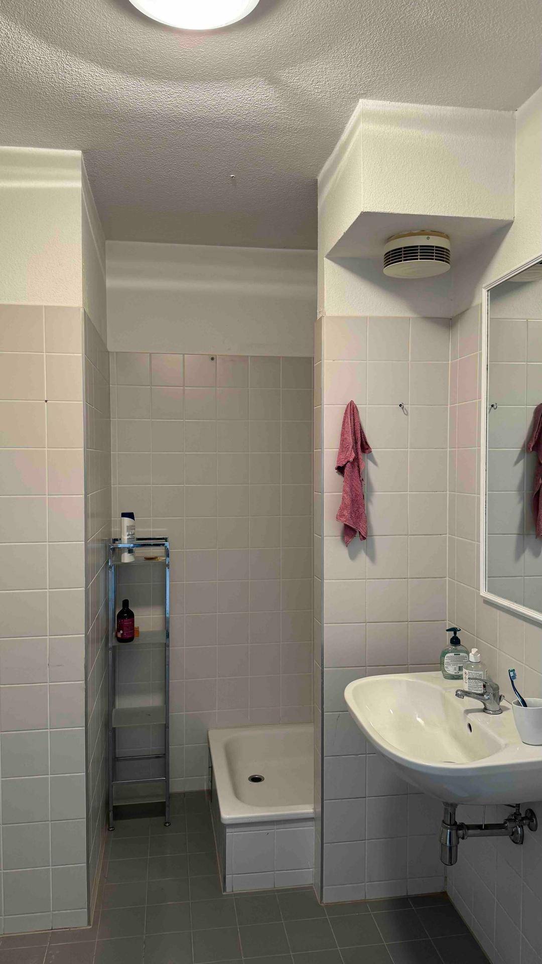 Badezimmer mit Duschwanne, Waschbecken und hellen Wandfliesen, funktional und gut beleuchtet.