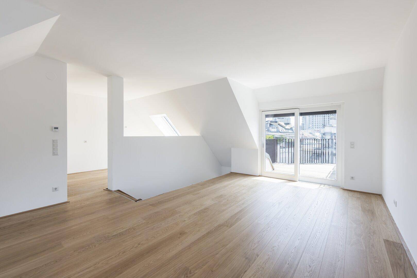 Heller Raum mit Holzboden, Zugang zu einem Balkon und schrägen Dachschrägen.