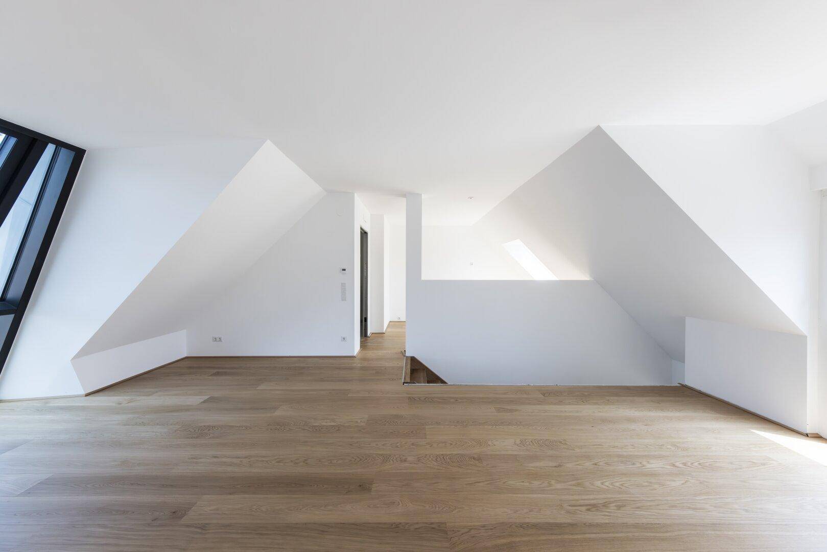 Geräumiger, leerer Raum im Dachgeschoss mit Holzboden und schrägen Wänden.