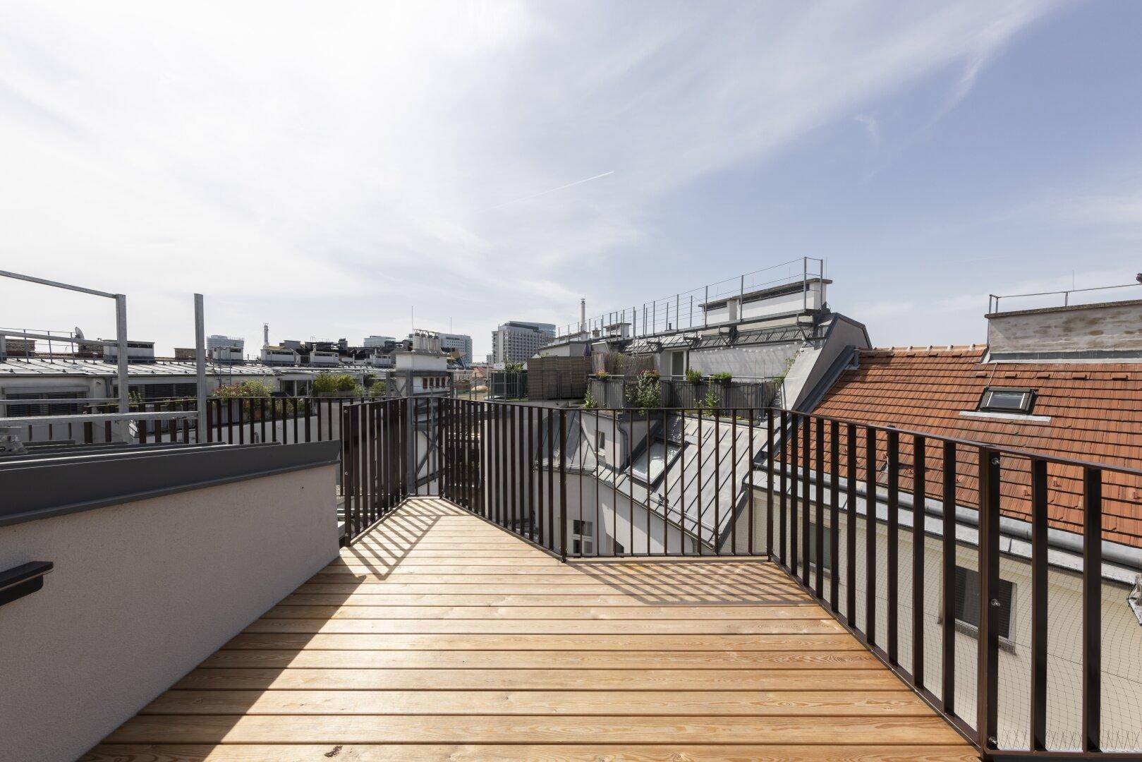 Dachterrasse mit Holzboden und schwarzem Geländer bietet einen weiten Blick über die Stadt.