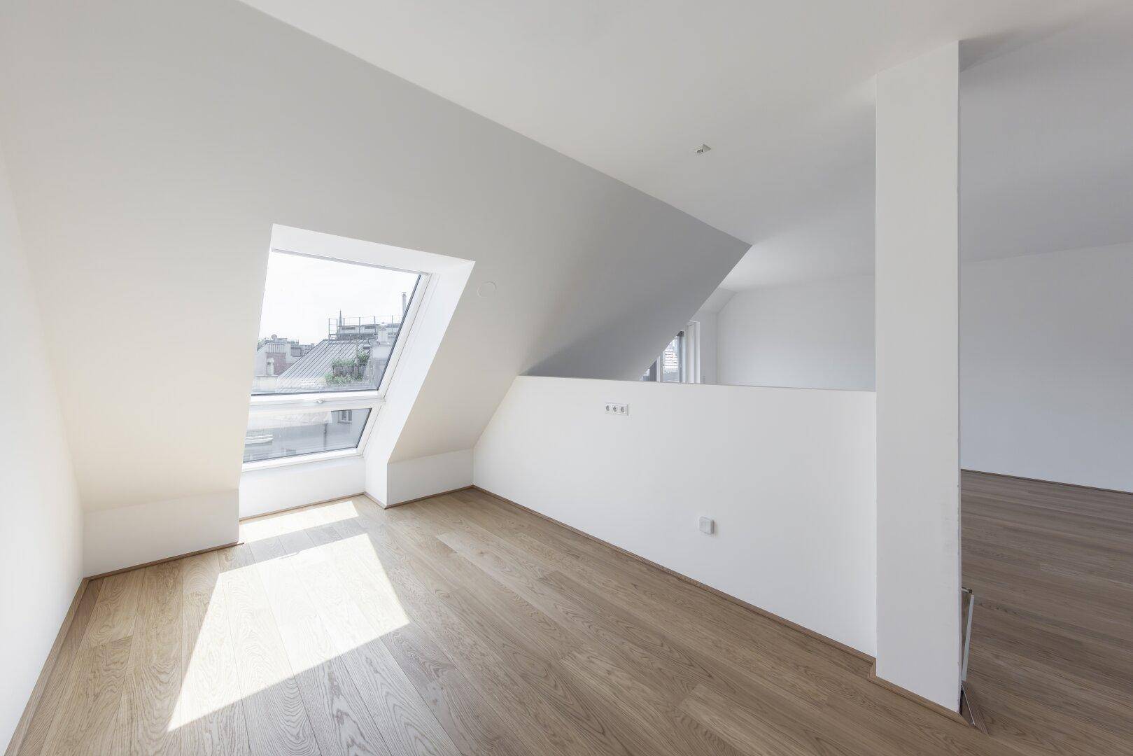 Lichtdurchfluteter Raum im Dachgeschoss mit Holzboden und großem Dachfenster.