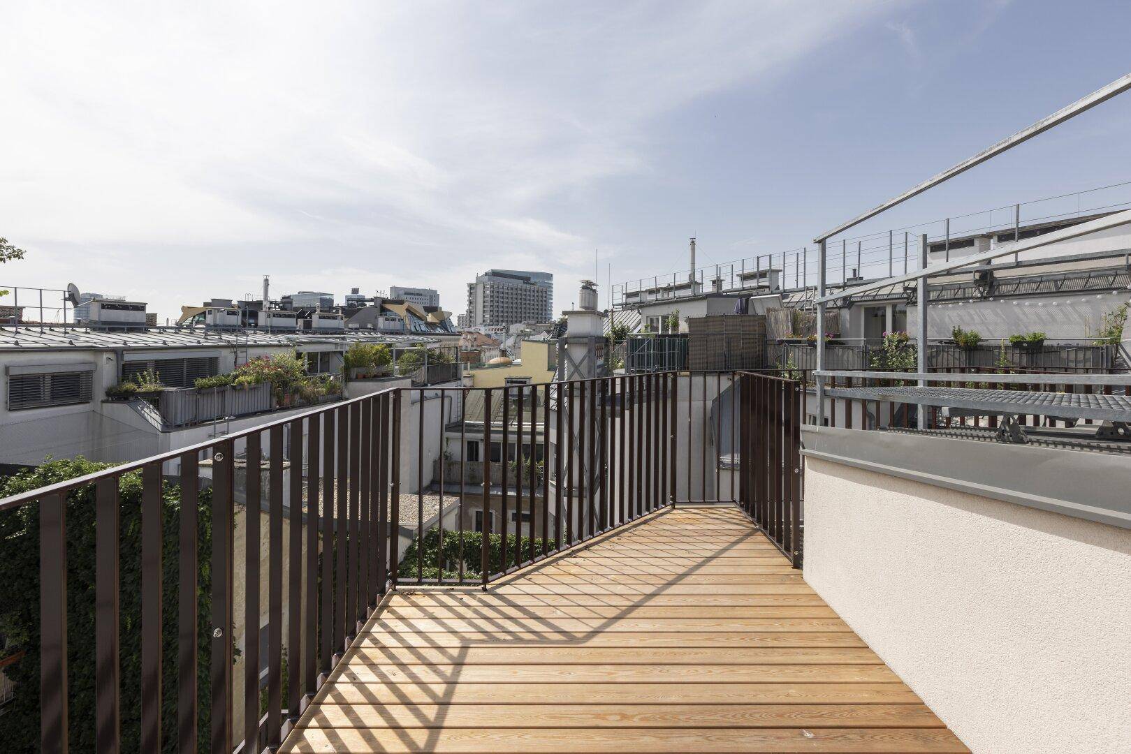 Geräumiger Balkon mit Holzboden und Metallgeländer bietet einen weiten Blick über die Stadt.