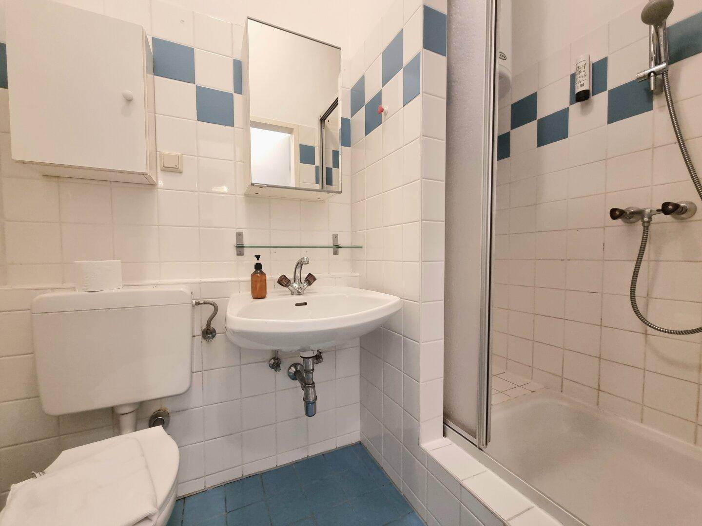 Badezimmer mit Dusche, WC, Waschbecken und blauen Akzentfliesen.