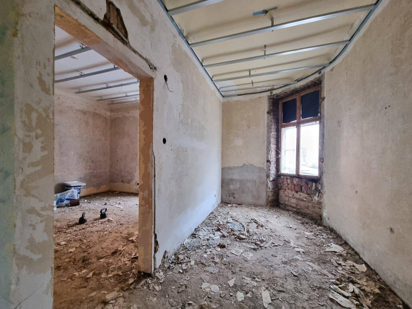 Renovierungsbedürftiger Raum mit freigelegten Wänden und Deckenkonstruktion in einem Altbau.