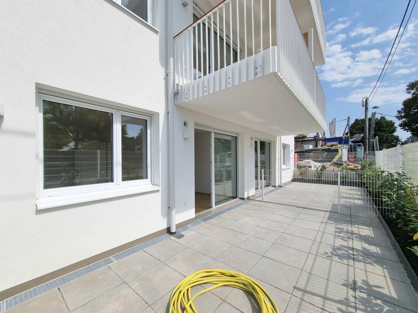 Moderne Gebäudefassade mit großer Terrasse und Balkon im Obergeschoss.