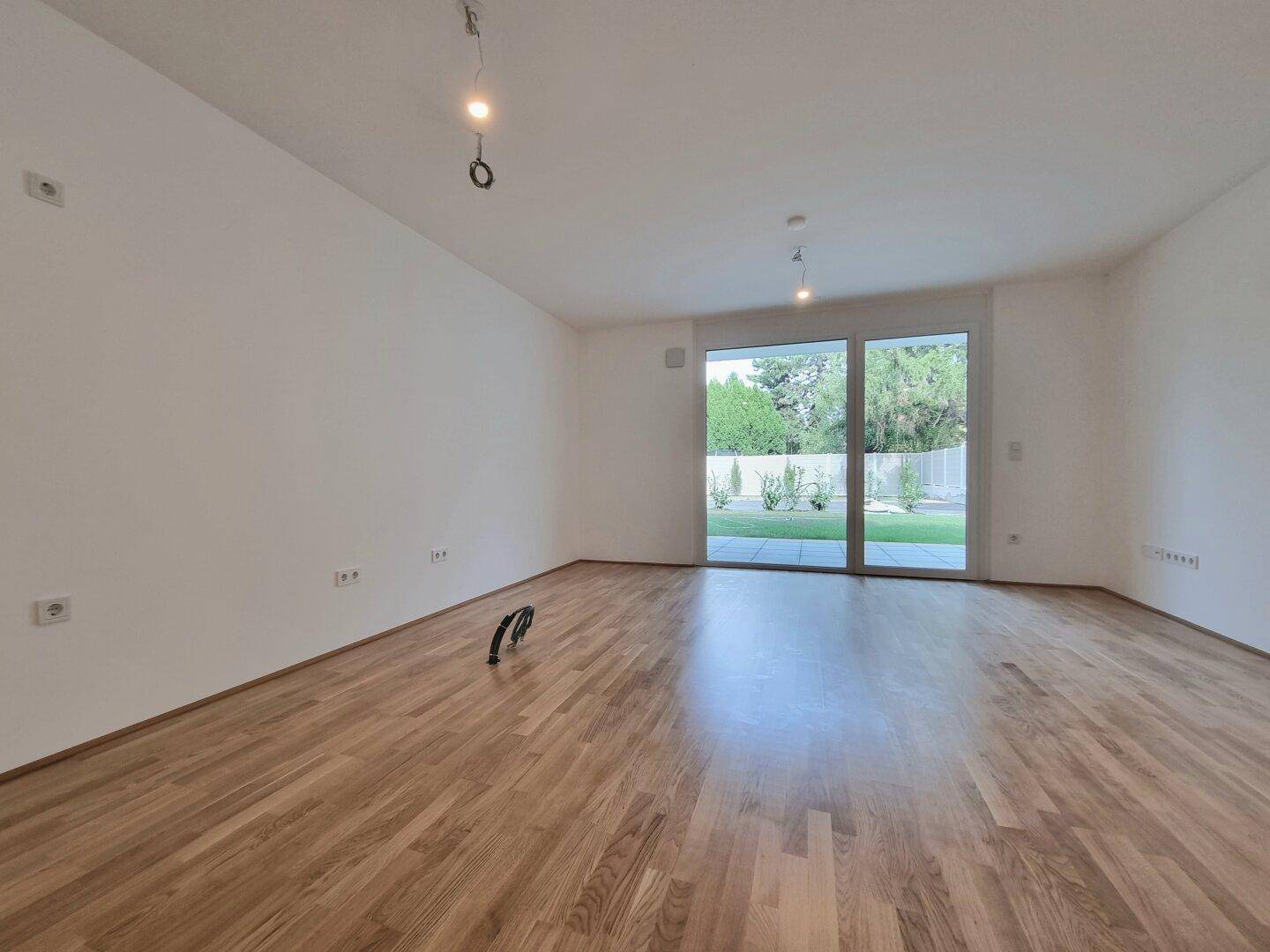 Geräumiges Wohnzimmer mit Holzboden und viel Tageslicht durch die Terrassentür.