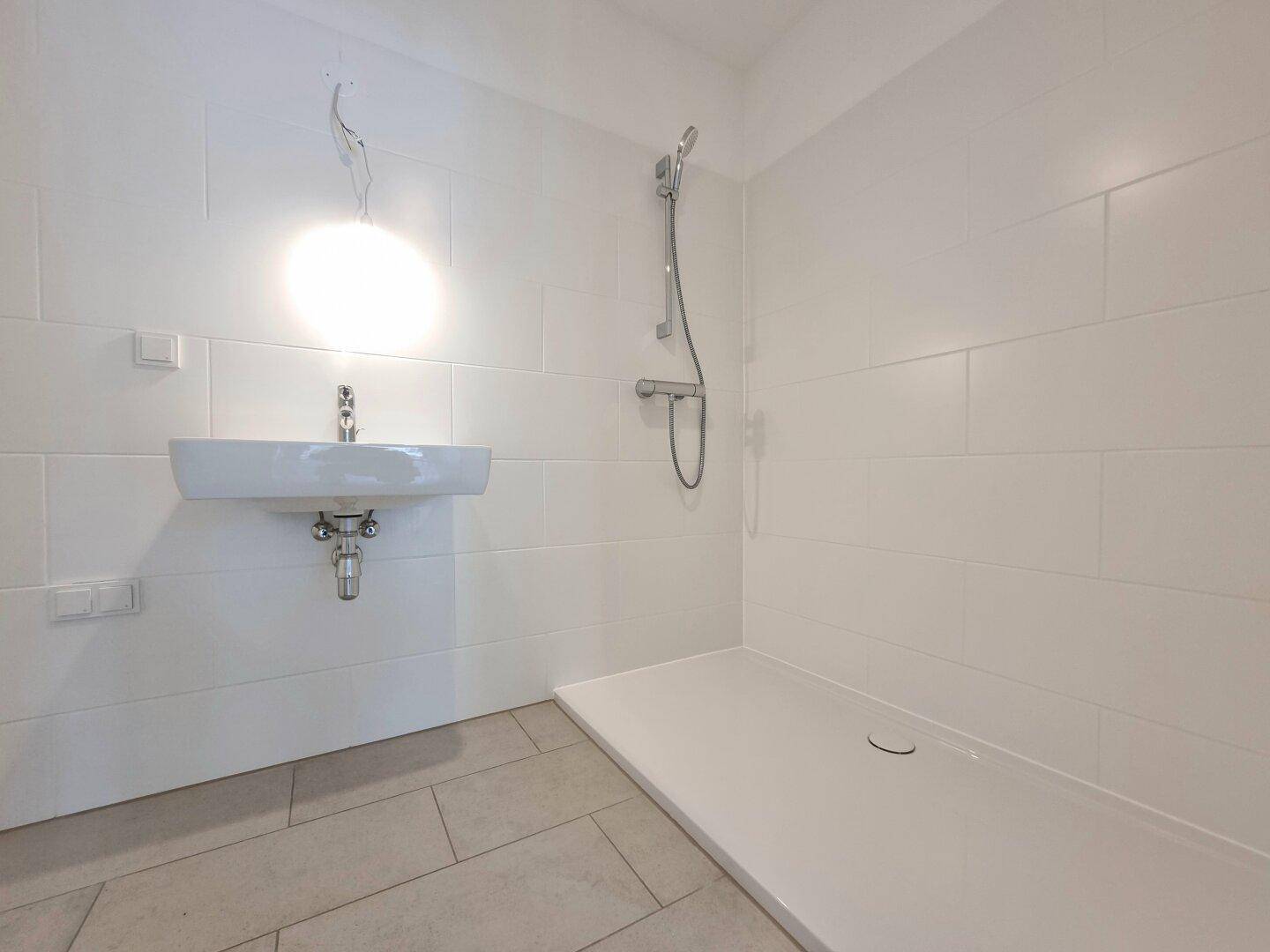 Modernes Badezimmer mit ebenerdiger Dusche, weiß gefliesten Wänden und hellem Boden.