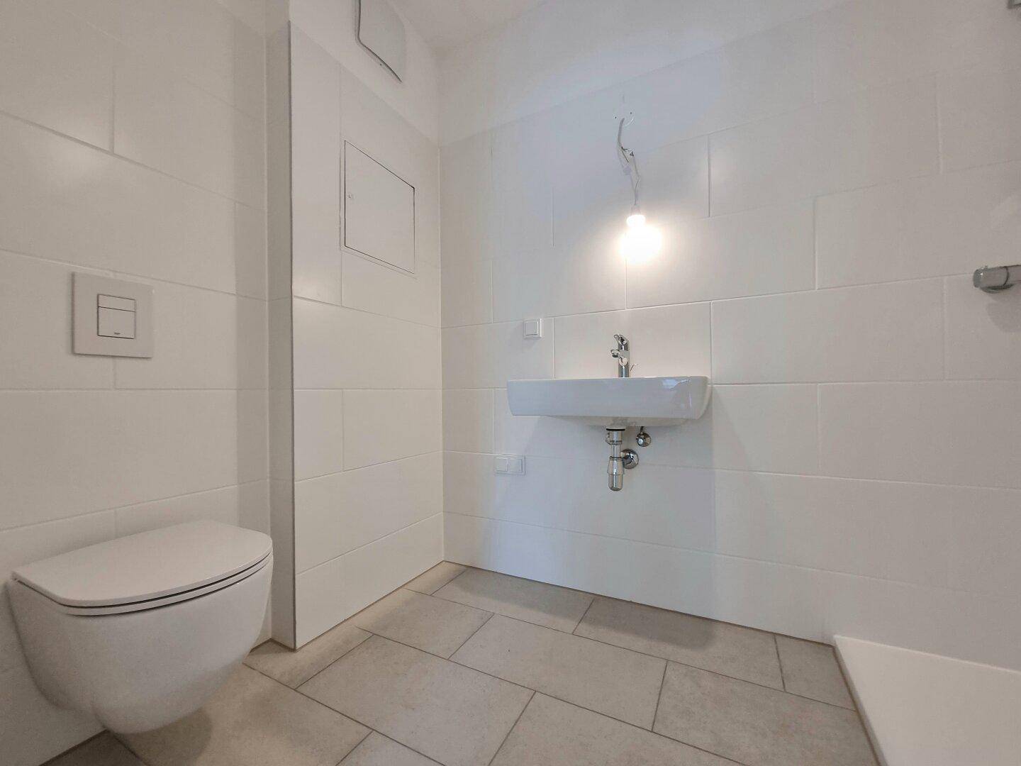 Zeitgemäßes Badezimmer mit wandhängendem WC, Waschbecken und weißen Fliesen.