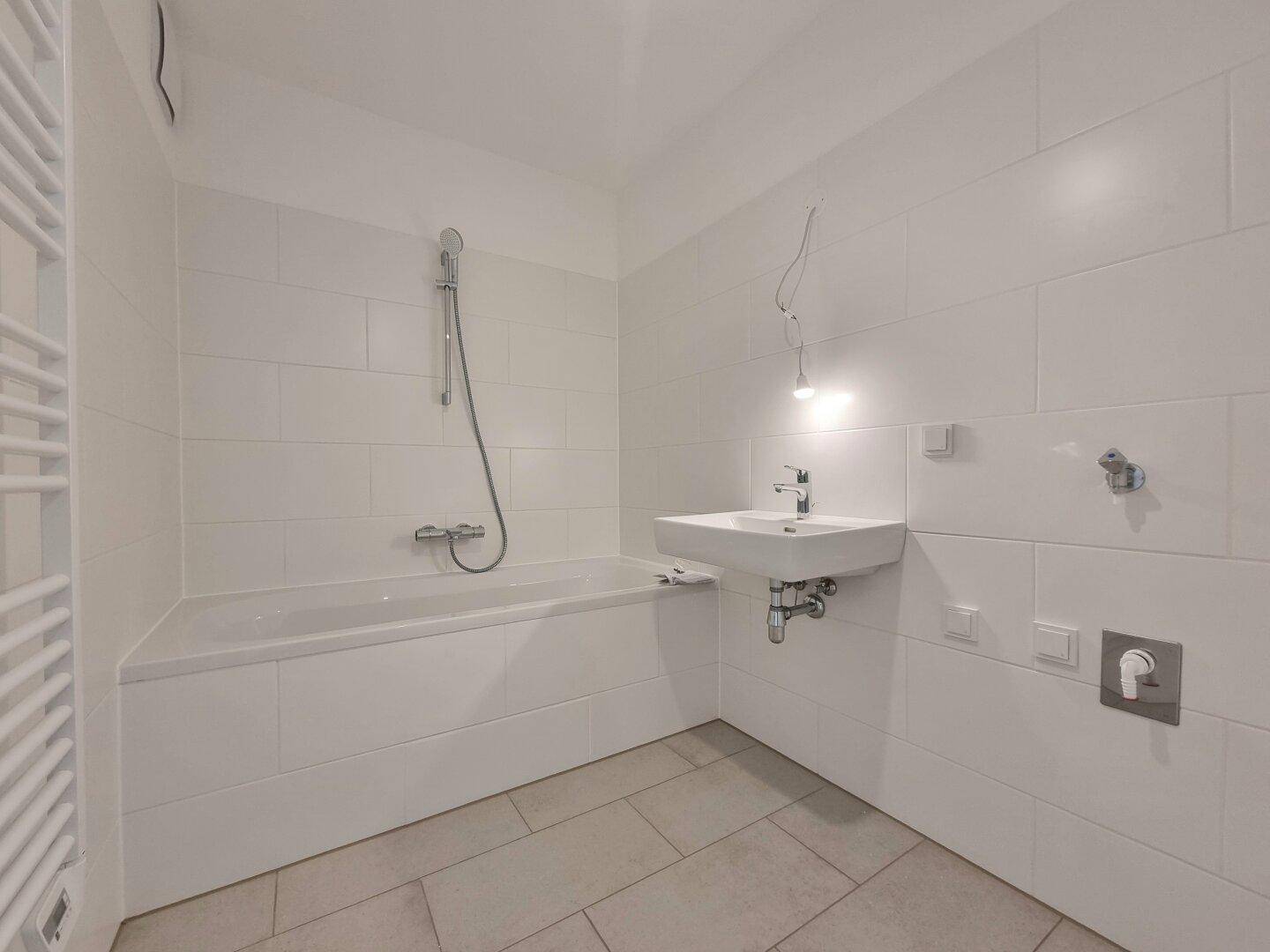 Helles Badezimmer mit Badewanne, Waschbecken und weißen Wandfliesen.