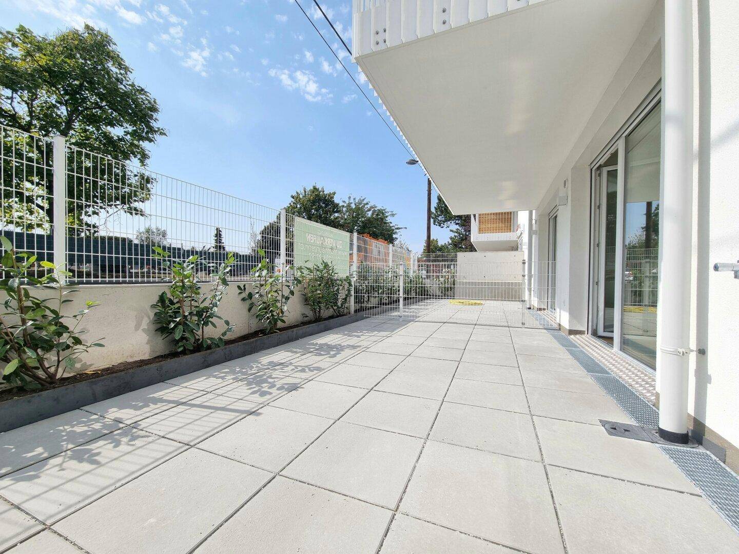 Lange, gepflasterte Terrasse entlang des Gebäudes mit Blick ins Grüne.