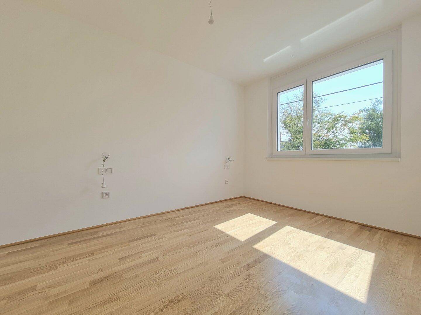 Helles Schlafzimmer mit Holzboden und Fenster, das viel Sonnenlicht in den Raum lässt.