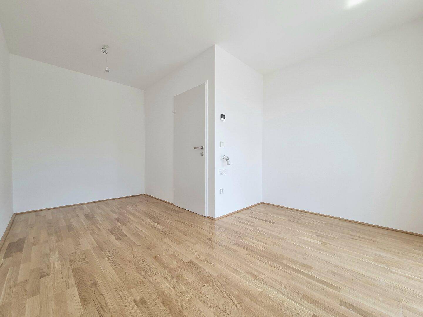 Leeres Zimmer mit hellem Holzboden und weißen Wänden, bereit für individuelle Gestaltung und Nutzung.