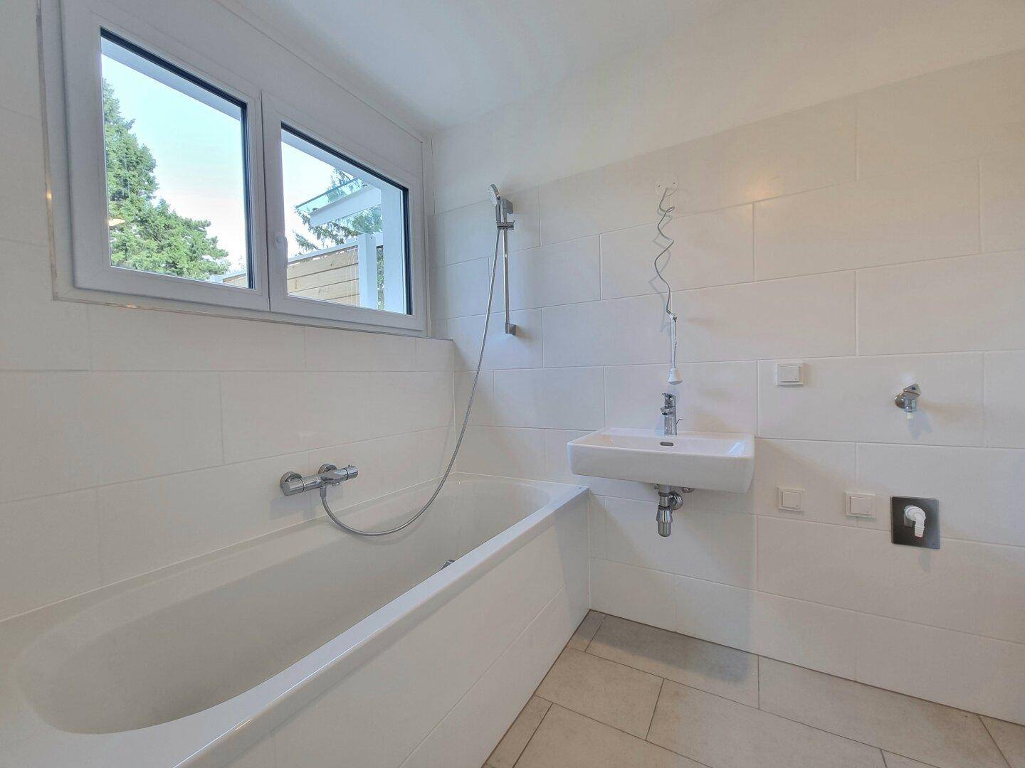 Modernes Badezimmer mit Badewanne, Waschbecken und Fenster für Tageslicht.