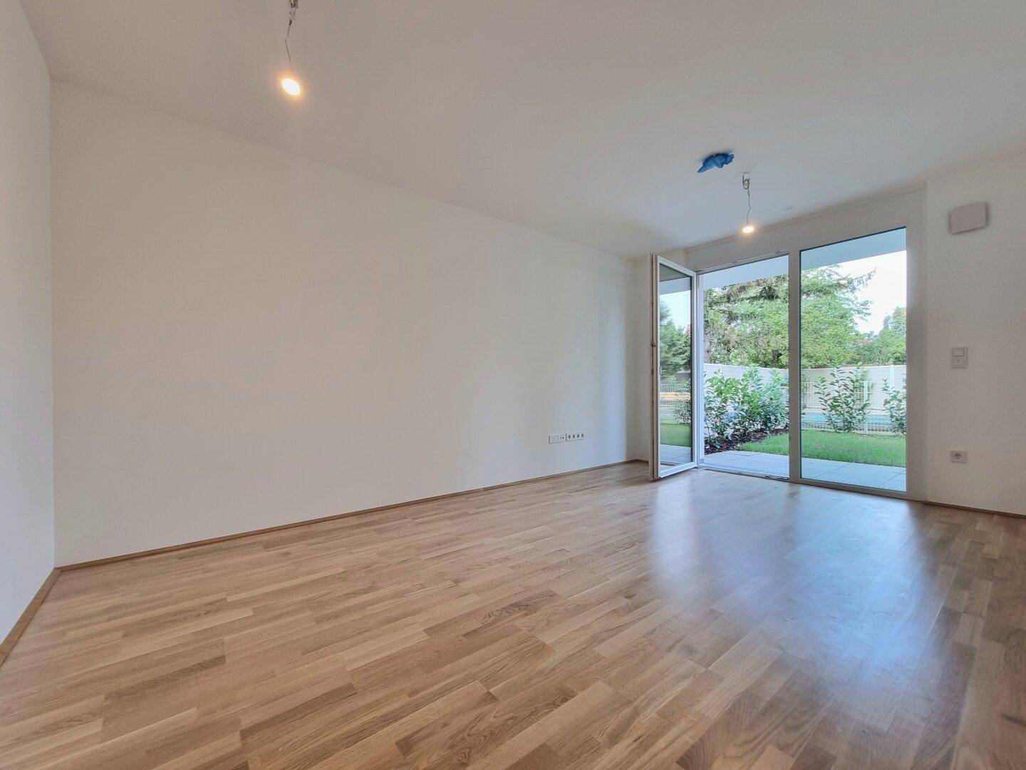 Geräumiges, unmöbliertes Wohnzimmer mit großen Fenstern und Blick ins Grüne.