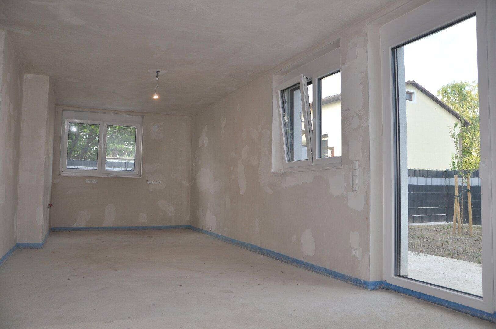 Geräumiger, unfertiger Innenraum mit Fenster und Tür, ideal für individuelle Gestaltung.